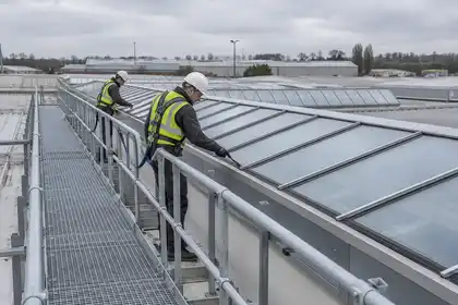 Technicians inspecting industrial rooflight seals from a guarded access walkway