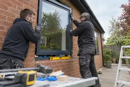 Two fitters setting a black aluminium window into a brick opening